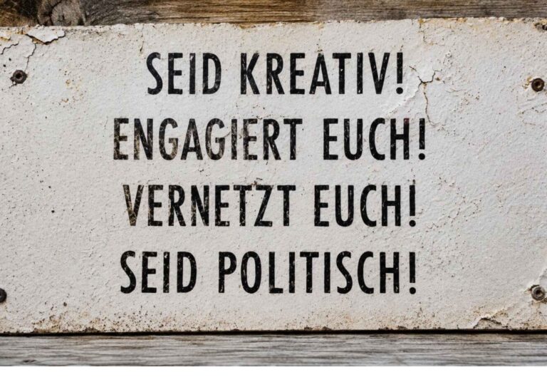 Altes verwittertes Schild an einer Holzwand mit der Aufschrift: „Seid kreativ! Engagiert euch! Vernetzt euch! Seid politisch!“